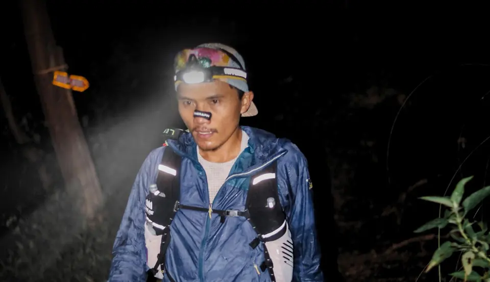 Pelari berlampu kepala di jalur hutan saat gelap