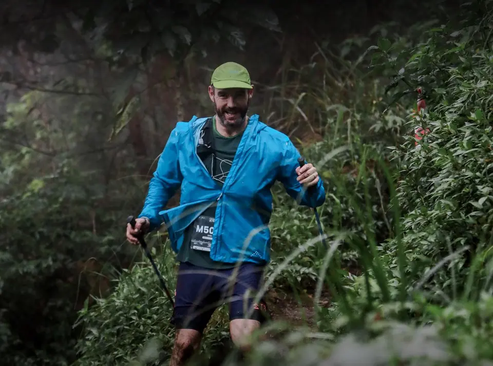 Pelari berjaket biru dengan tongkat menuruni jalur hutan Lawu